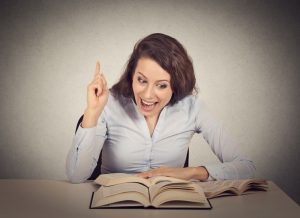 Smiling excited woman reading book has idea pointing with finger up