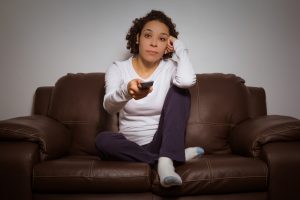 Serious woman holding remote control and watching TV