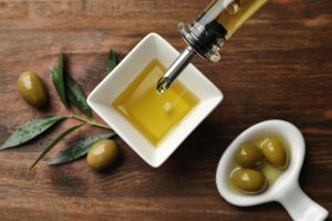 Pouring fresh olive oil into bowl on table, top view