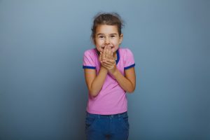 baby girl oops hand to mouth on gray background