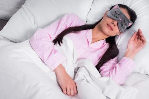 portrait of woman in pink pajamas and sleeping mask sleeping in bed at home