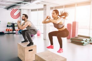 A picture of slim and well-built young man and woman doing jumps on platform. It is a hard exercise but they are doing it successful and with dilligence.